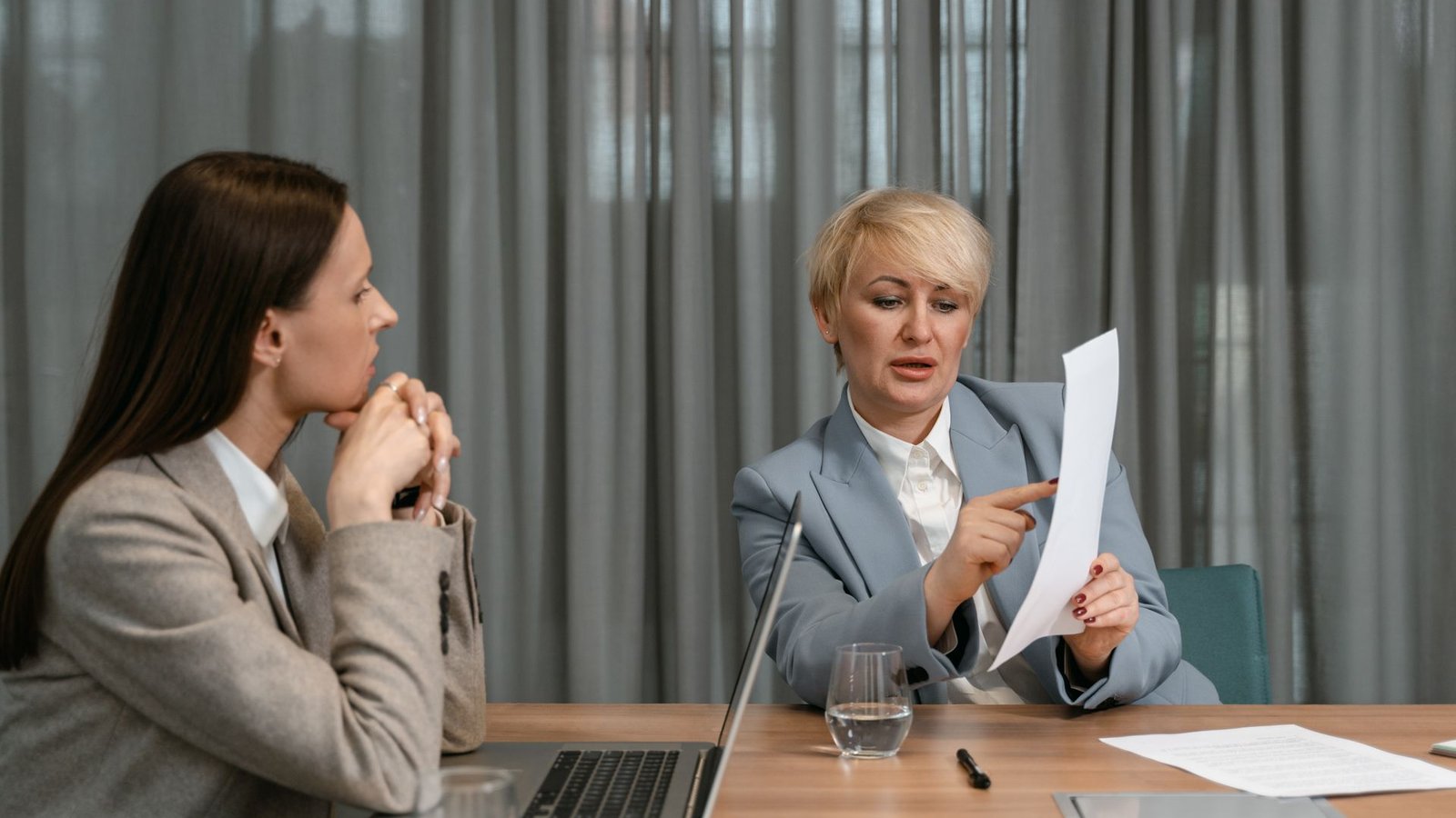An experienced woman and a younger colleague reviewing a document together across a meeting table
